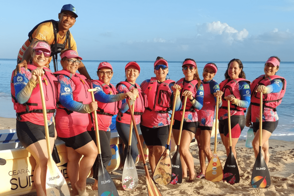 Grupo com coletes salva-vidas rosas e remos reunido na praia