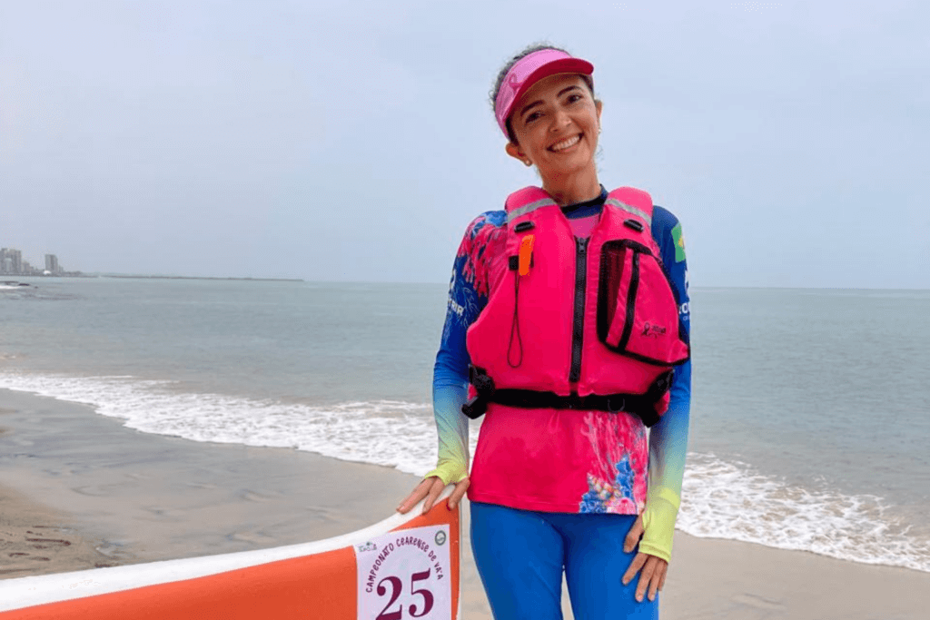 Participante usando colete salva-vidas rosa ao lado de caiaque na praia