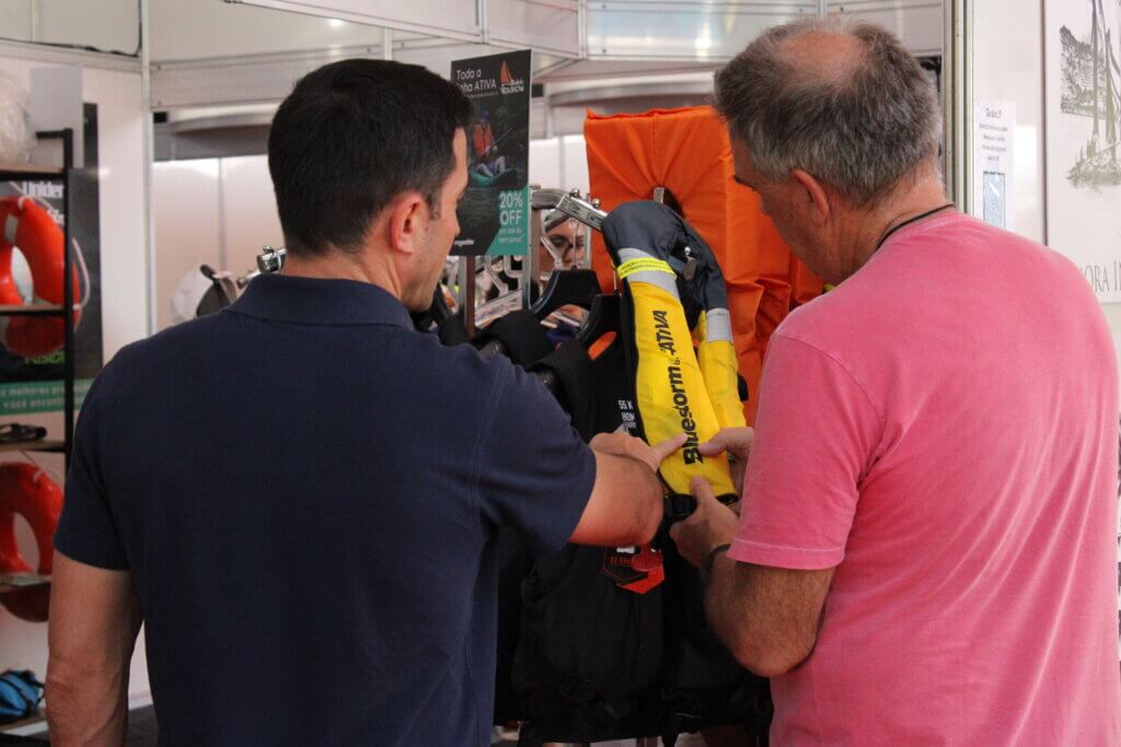 Participantes observando coletes salva-vidas em estande da Vela Show 2024