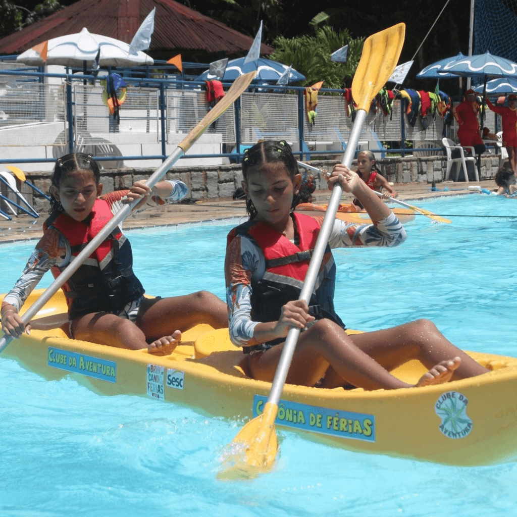 Duas crianças remando em caiaque amarelo na piscina