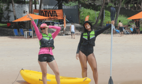 Participantes com coletes salva-vidas ao lado de caiaque amarelo na praia