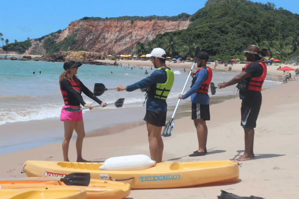 Grupo recebendo orientações ao lado de caiaques na praia