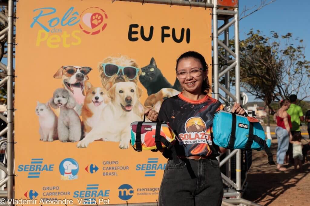 Participante do Rolê dos Pets segurando produtos Ativa Pet diante do painel do evento