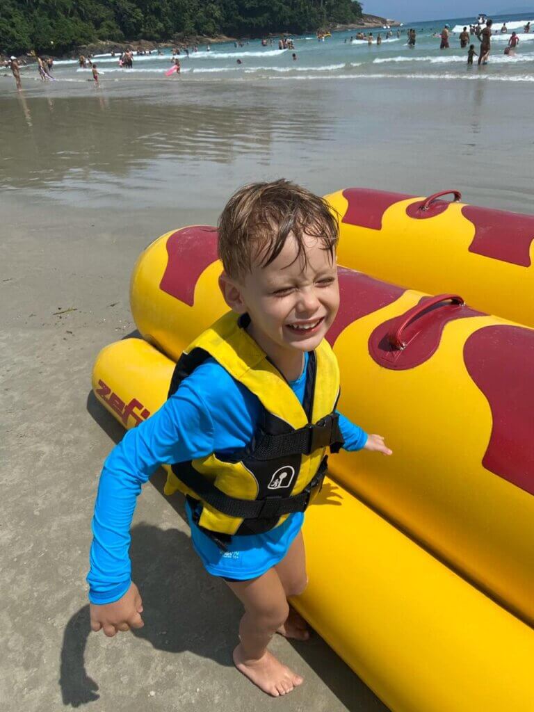 Criança na praia usando colete salva-vidas amarelo e preto