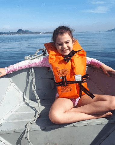 Criança em embarcação usando colete salva-vidas laranja
