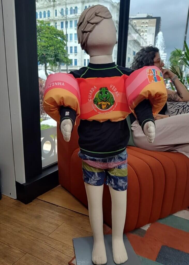 Manequim infantil usando colete salva-vidas e boias de braço