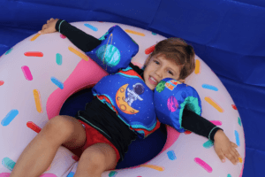Criança usando colete infantil da coleção Pequenos Universos em boia inflável na piscina