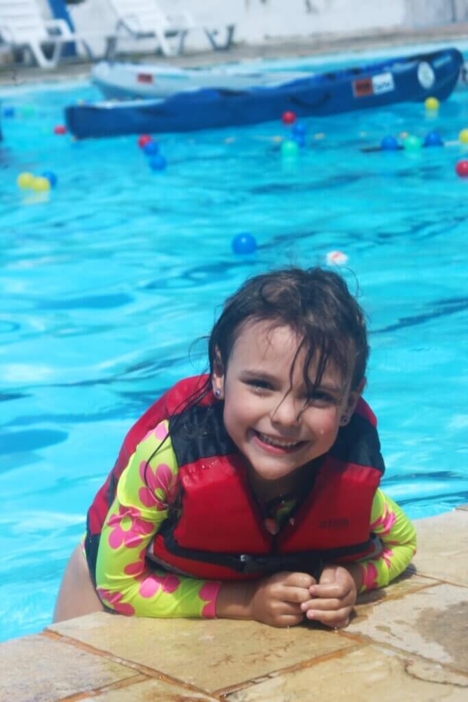 Criança na borda da piscina usando colete salva-vidas vermelho