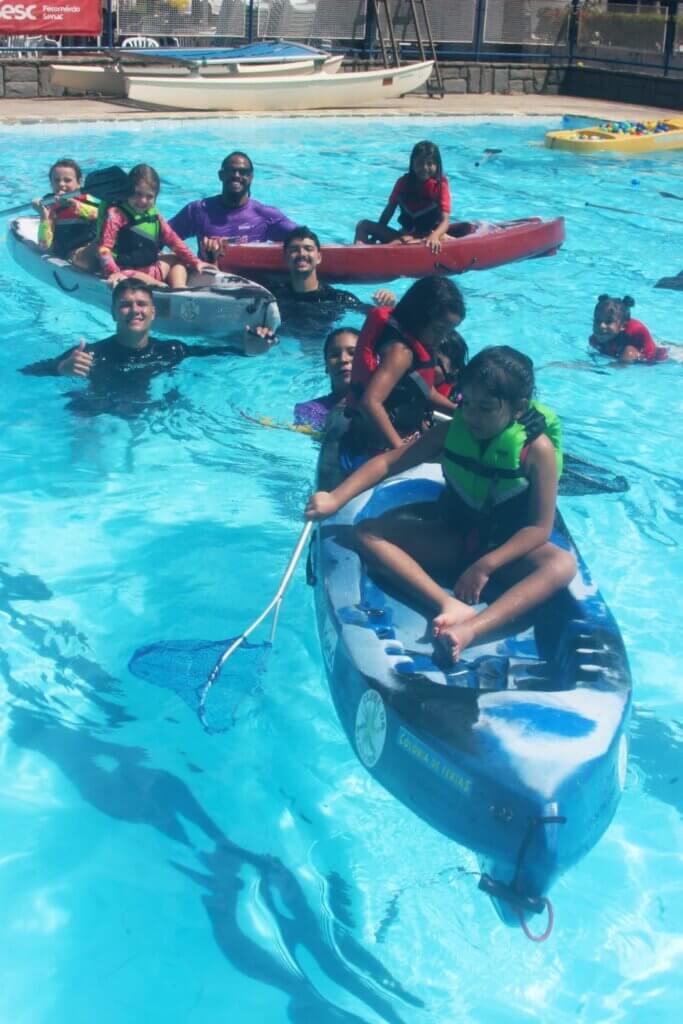 Participantes em atividade com caiaque dentro da piscina usando coletes salva-vidas