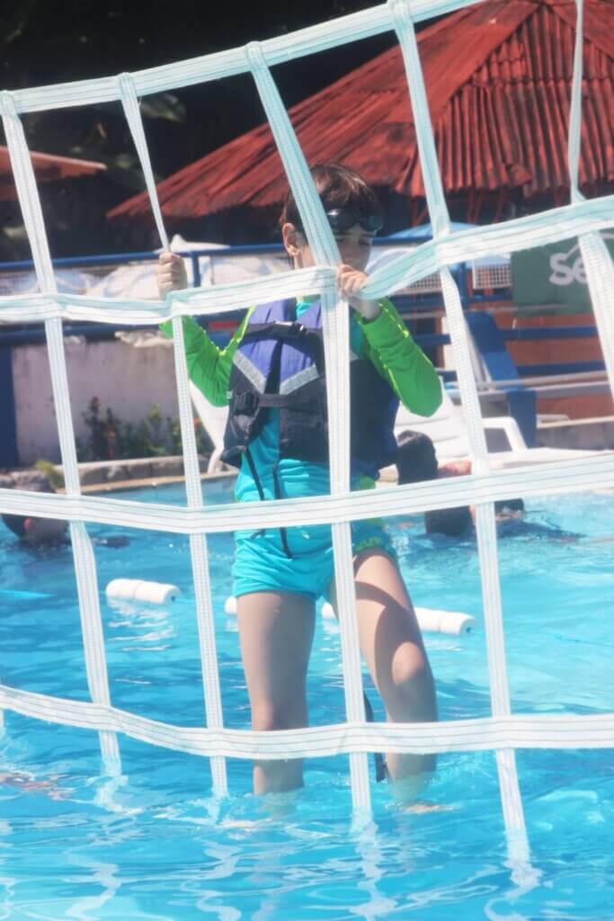 Criança usando colete salva-vidas em circuito de obstáculos sobre piscina